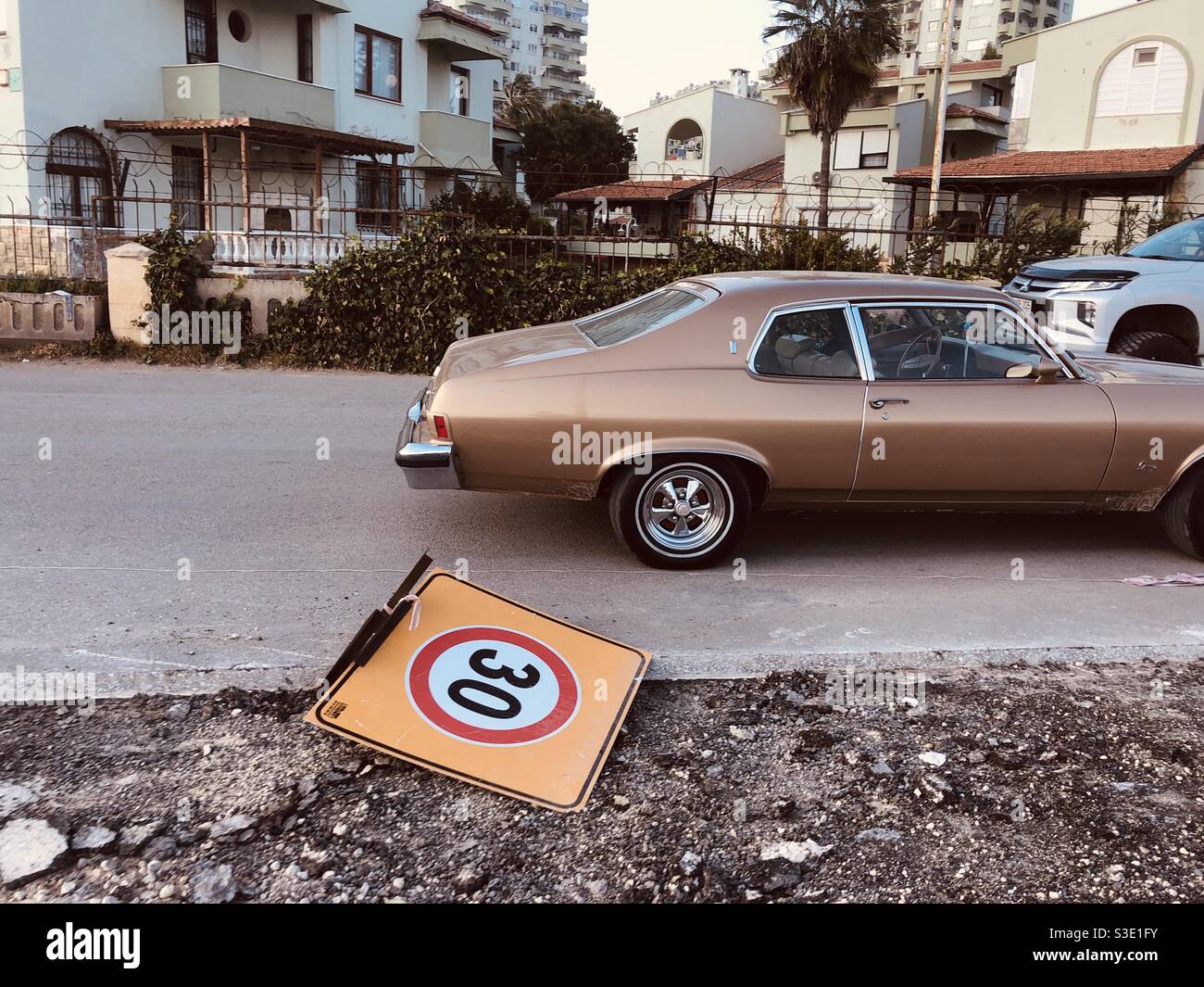 Auto d'epoca che passa accanto a un cartello stradale abbattuto - Immagine stock catturata con smartphone