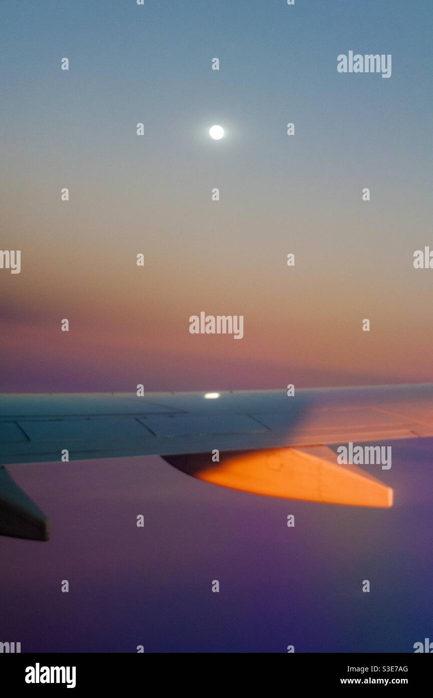 Moonrise sul Pacifico, sopra il bagliore del tramonto, avvicinandosi all'isola di Maui, Hawaii, USA. Luna piena riflessa sull'ala, fotografata da un sedile a finestra. 10000 metri. Foto Stock