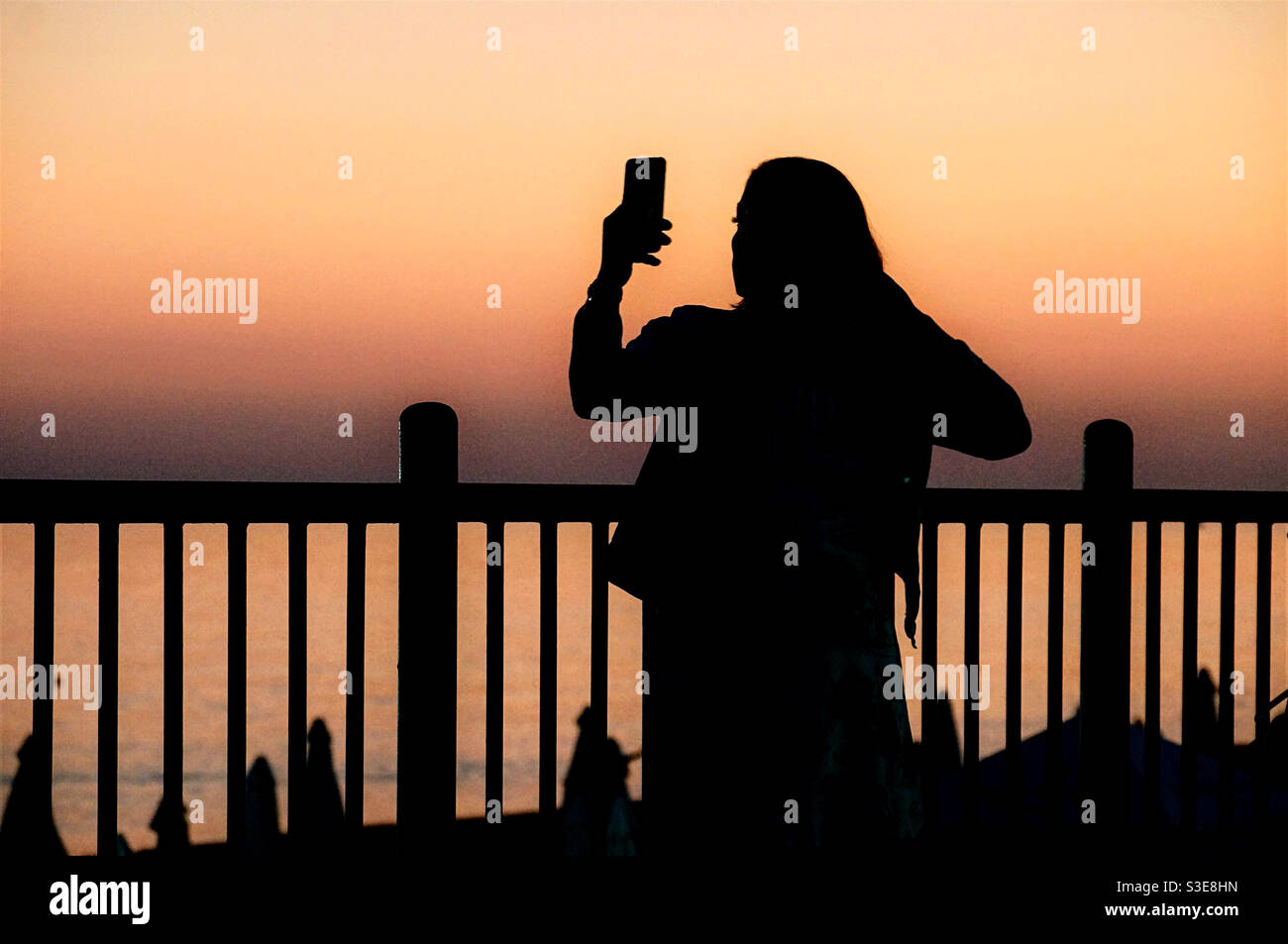 Silhouette di una ragazza con uno smartphone sullo sfondo del cielo serale - Immagine stock catturata con smartphone