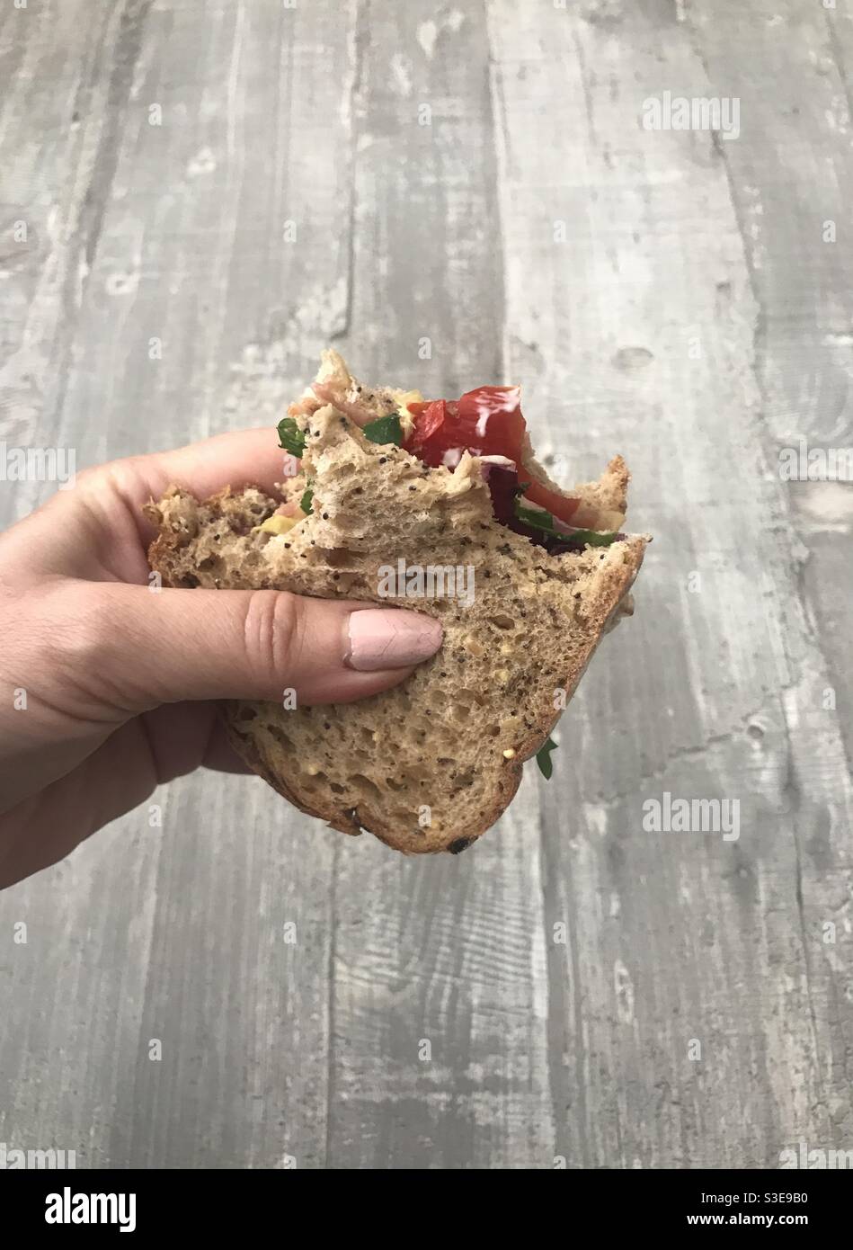 Donna che tiene un panino seminato di pancetta croccante, lattuga e pomodoro Foto Stock