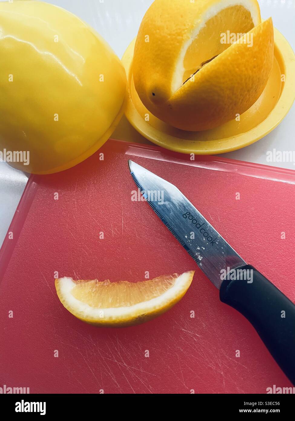 Primo piano di un limone Meyer a fette su un arancio tagliere con un coltello di taglio molto affilato Foto Stock