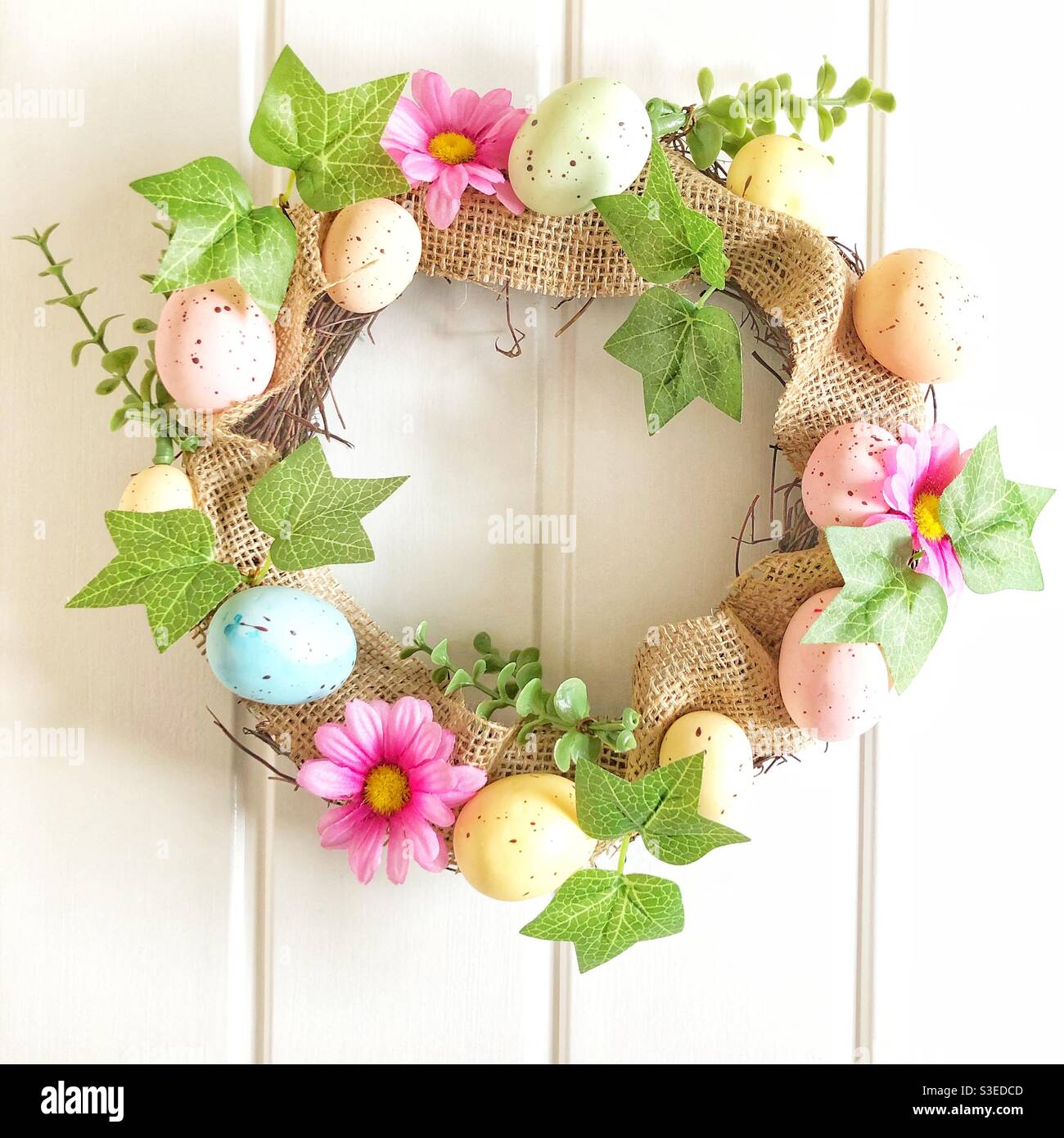 Una colorata corona di Pasqua con uova di Pasqua e primavera fiori su sfondo bianco Foto Stock