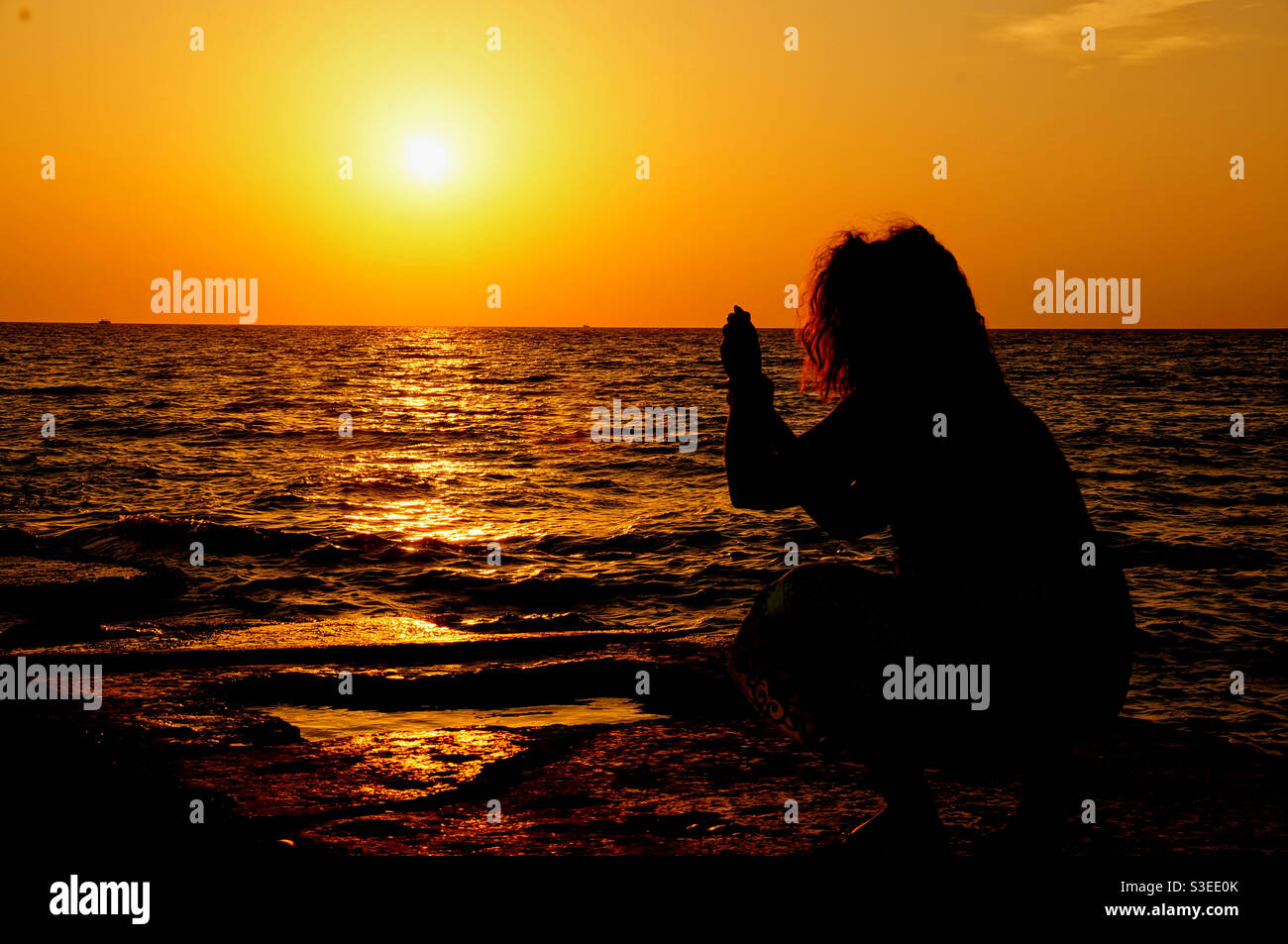 Silhouette di una ragazza con i capelli lussureggianti che scattano le foto di il tramonto sul mare Foto Stock