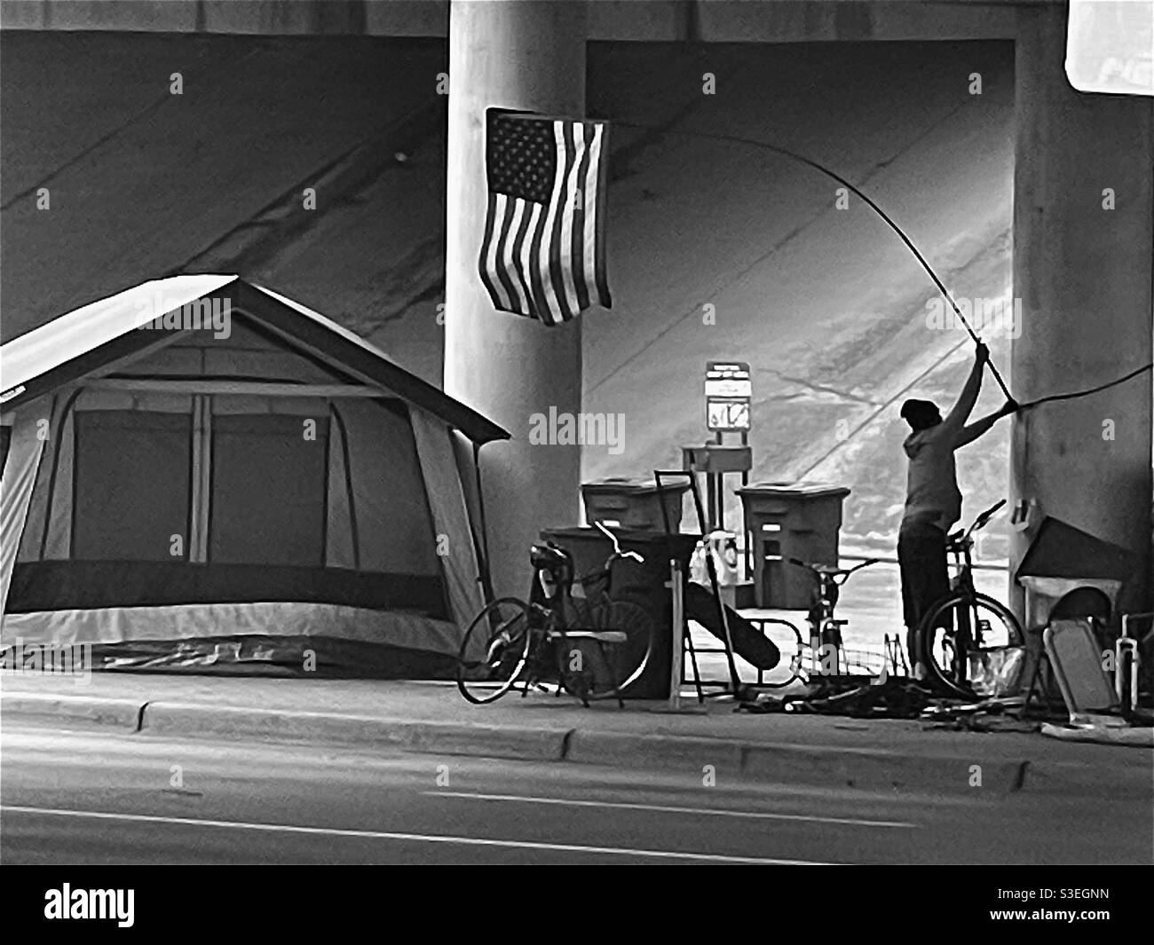 Un uomo senza casa mette una bandiera americana a un accampamento sotto un ponte ad Austin, Texas. Foto Stock