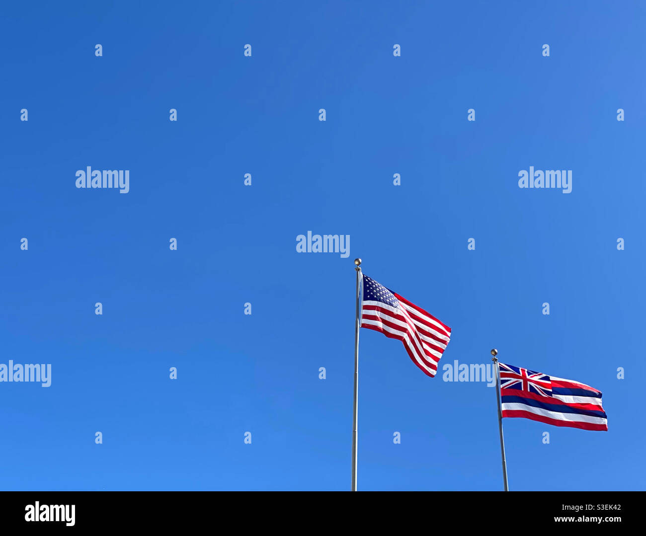 Bandiera degli Stati Uniti e bandiera dello stato delle Hawaii fianco a fianco contro un cielo blu senza nuvole Foto Stock