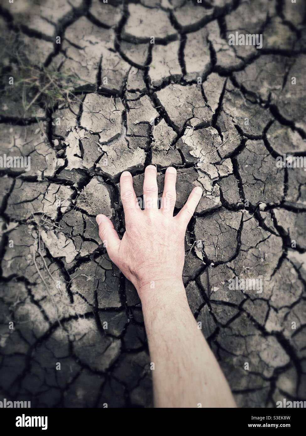 Una mano umana che raggiunge per acqua in un asciutto e. letto del fiume incrinato Foto Stock