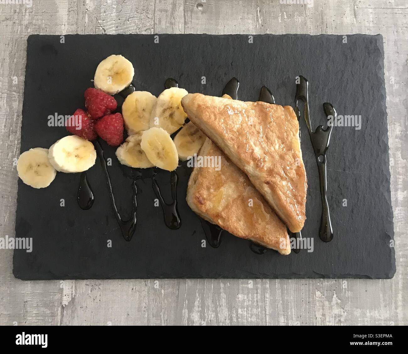 Toast alla cannella alla francese servito con lamponi e banane a fette e. condito con sciroppo d'acero Foto Stock