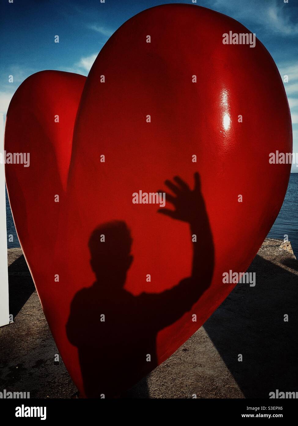 Ombra di un uomo che agita la mano su un cuore a forma di cuore display Foto Stock