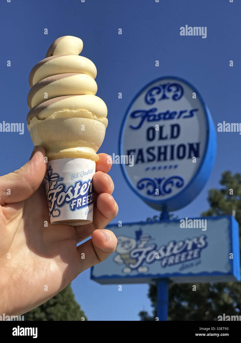 Burbank, CA / USA - 28 marzo 2021: Di fronte a un cartello Fosters Freeze,  una mano tiene un cono di gelato al cioccolato e alla vaniglia. Questa  catena di ristoranti della