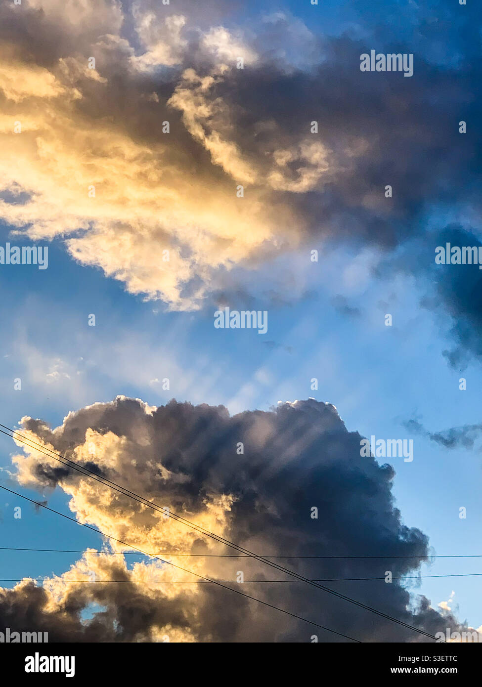 Raggi di luce solare che irradiano raggi di sole attraverso le nuvole bianche e grigie, cielo blu Foto Stock