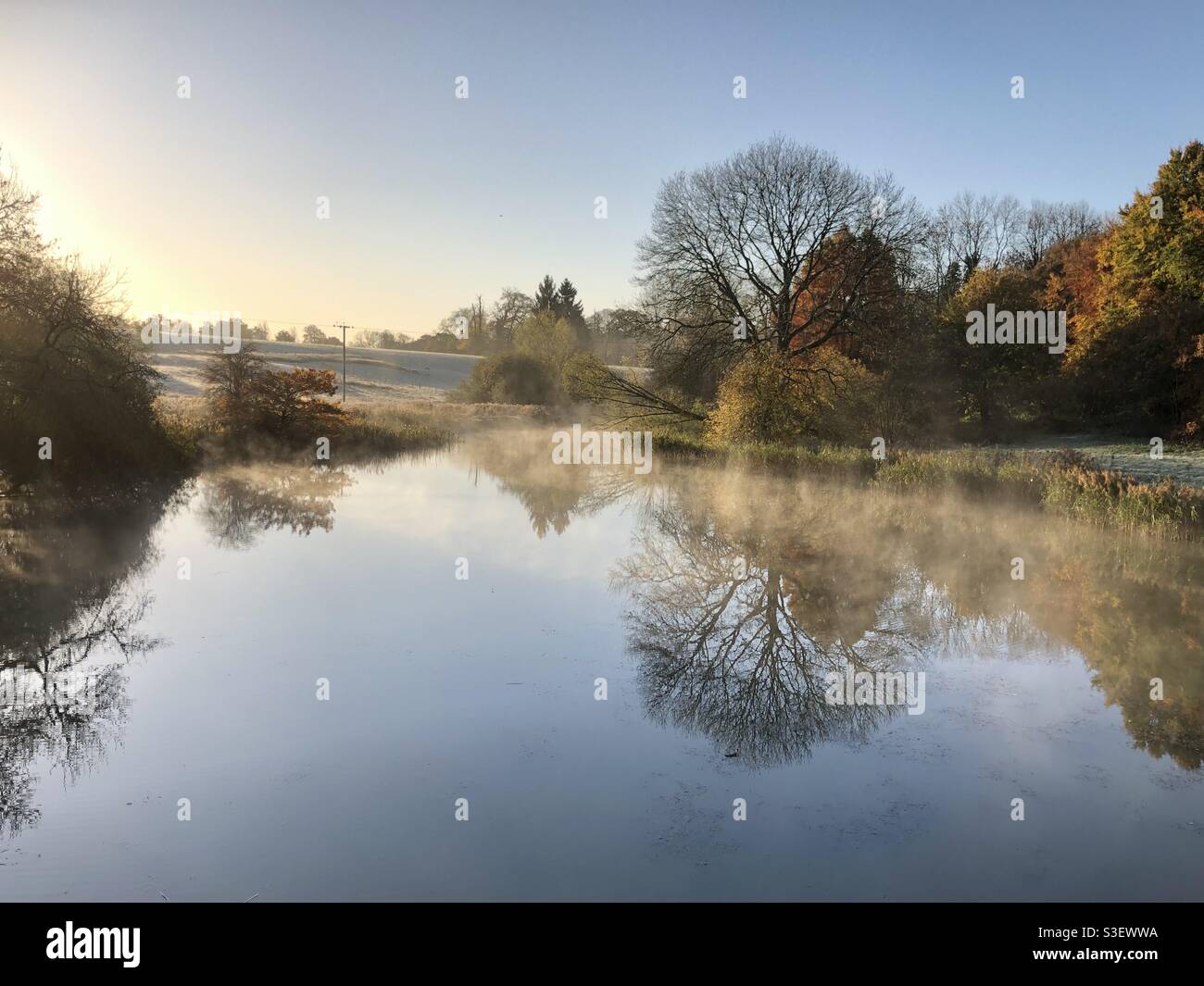 Paesaggio invernale che si affaccia su un lago in brina con nebbia misteriosa e sole luminoso. - Immagine stock catturata con smartphone