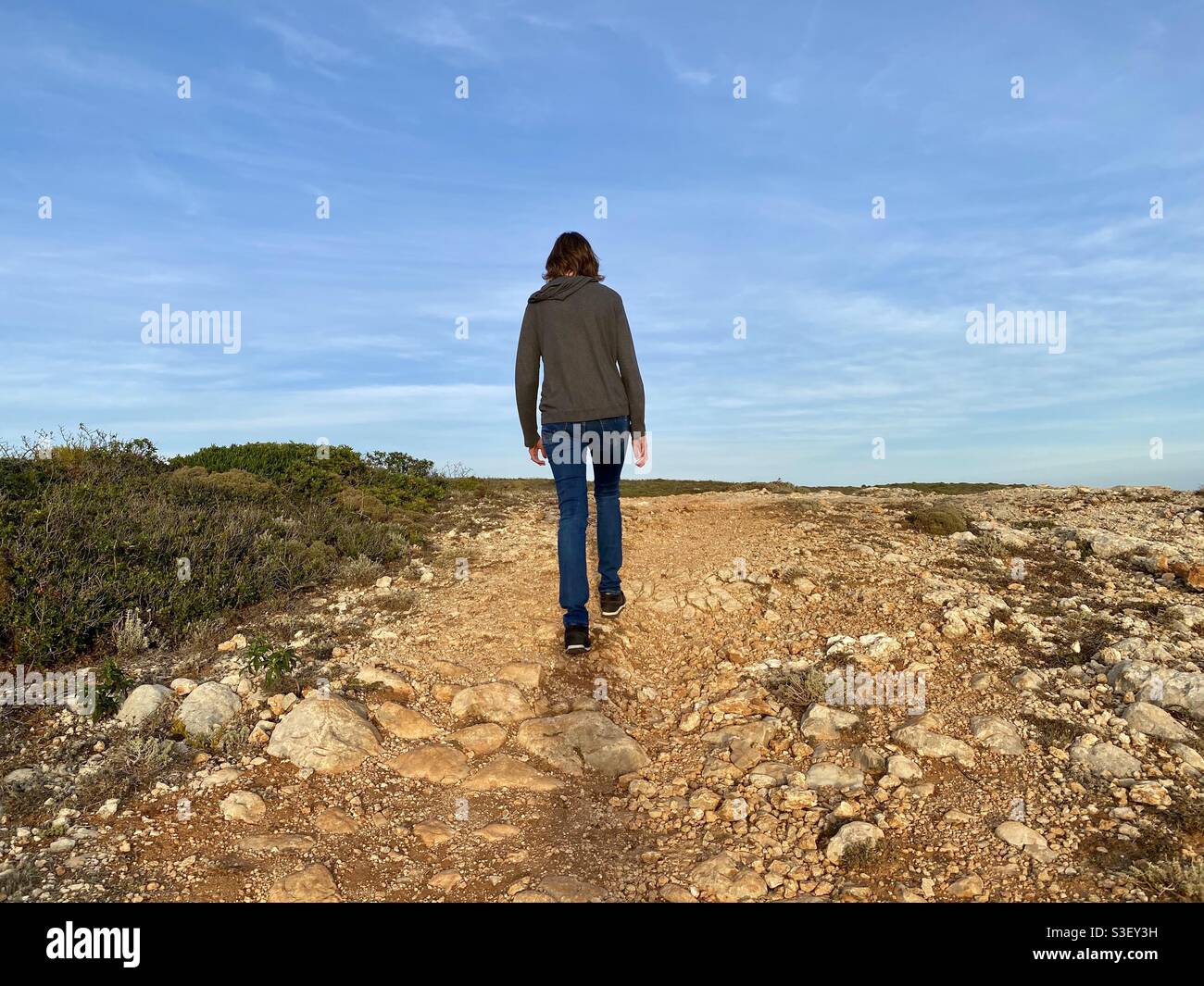 Vista posteriore della donna vestita di abbigliamento casual che cammina lungo un sentiero remoto Foto Stock