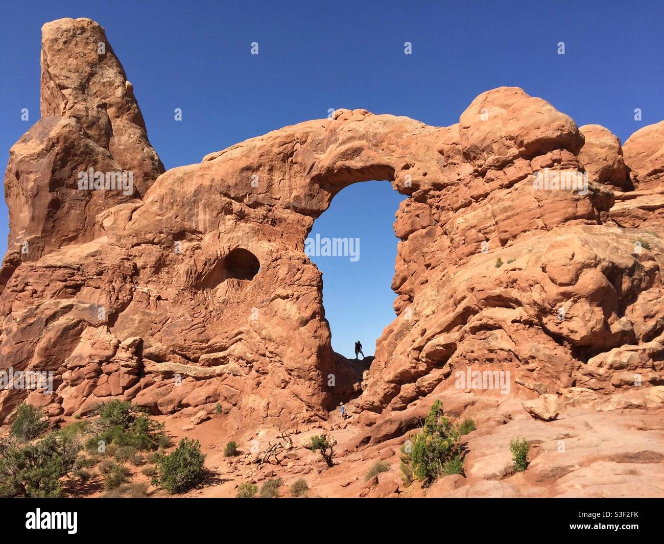 Un escursionista si trova in una silhouette contro il cielo blu nel Turret Arch, nel Parco Nazionale di Arches, Utah - Immagine stock catturata con smartphone