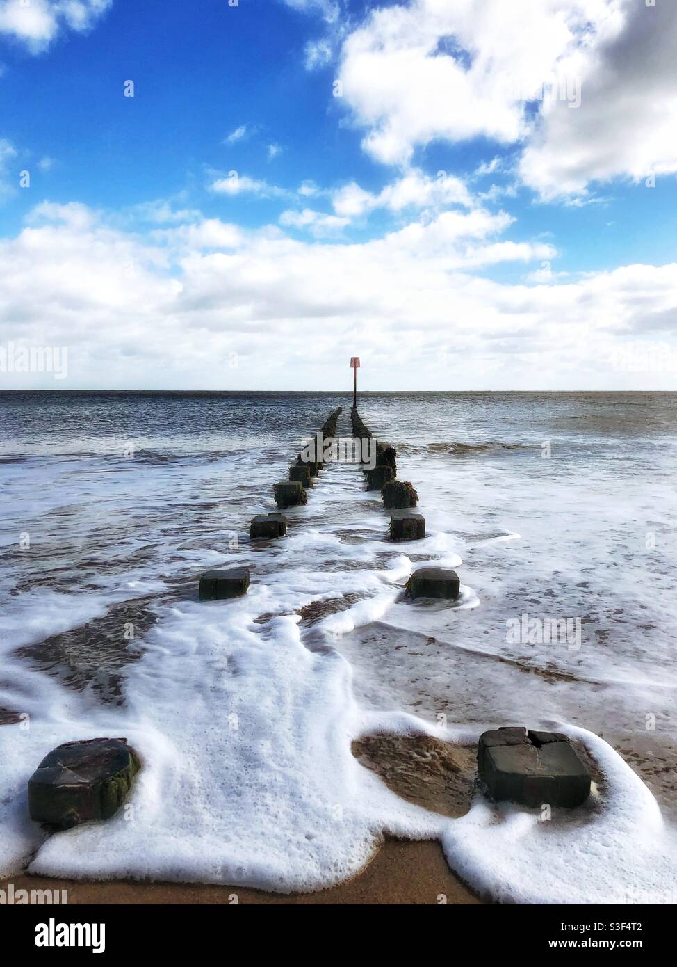 Colonne di legno che si estendono verso un posto di avvertimento su un Spiaggia di sabbia in una località balneare britannica Foto Stock