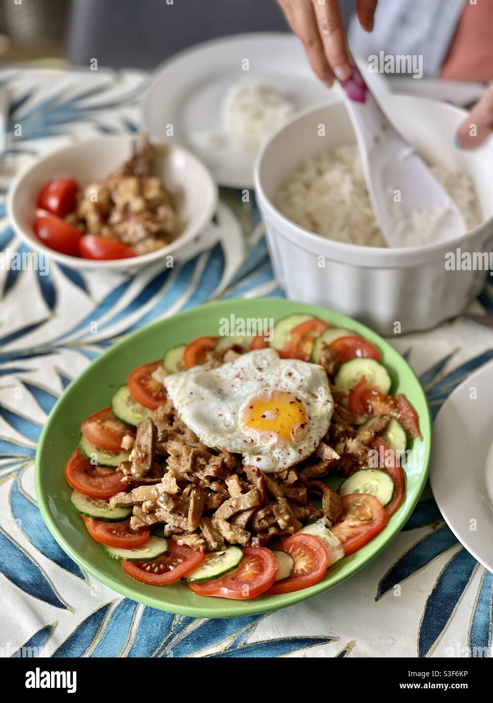 Donna filippina del sud-est asiatico prepara il riso sul piatto filippino di Sisig con pancia di maiale, il lato soleggiato dell'uovo e il contorno dei pomodori Foto Stock