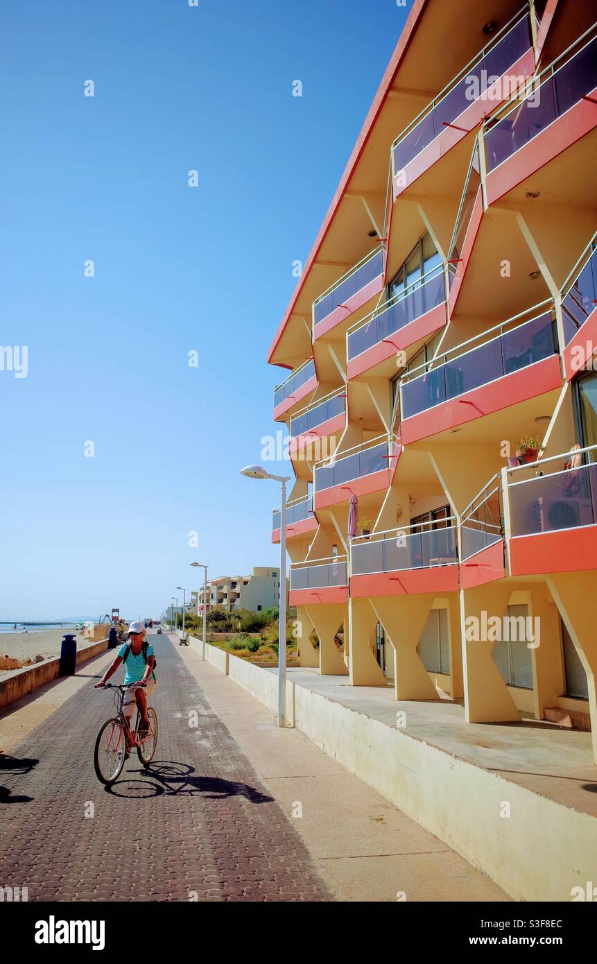 Una bicicletta turistica che passa accanto a un edificio arancione, rosso e blu lungomare su un percorso in bicicletta a Palavas les Flots vicino a Carnon plage e Montpellier, Occitanie, a sud della Francia Foto Stock