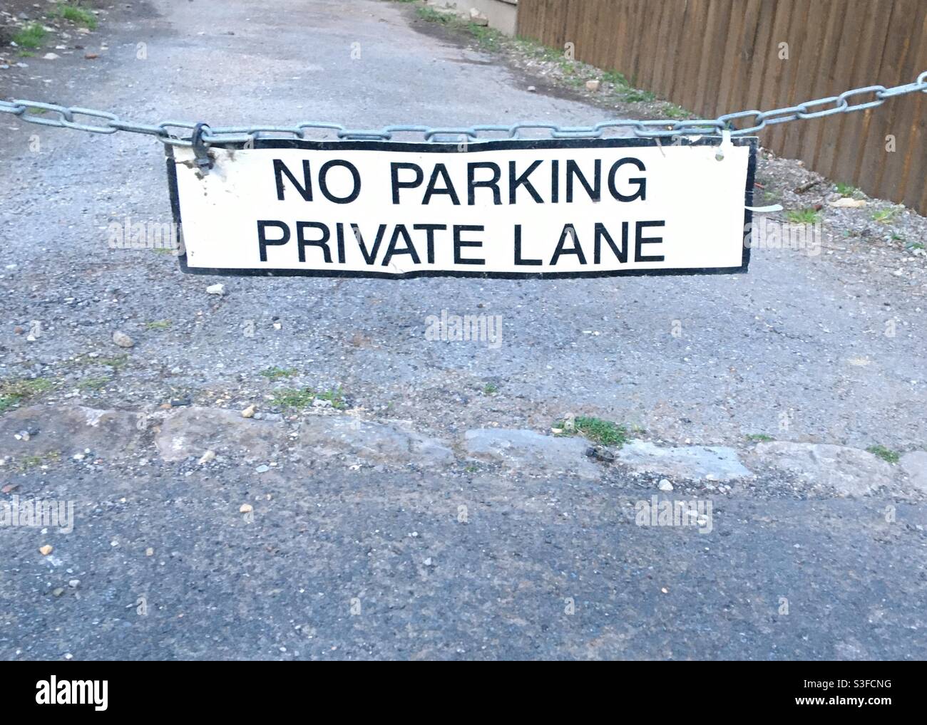 Un cartello bianco e nero che dice ‘Nessun parcheggio. Private Lane’, appeso a una catena Foto Stock