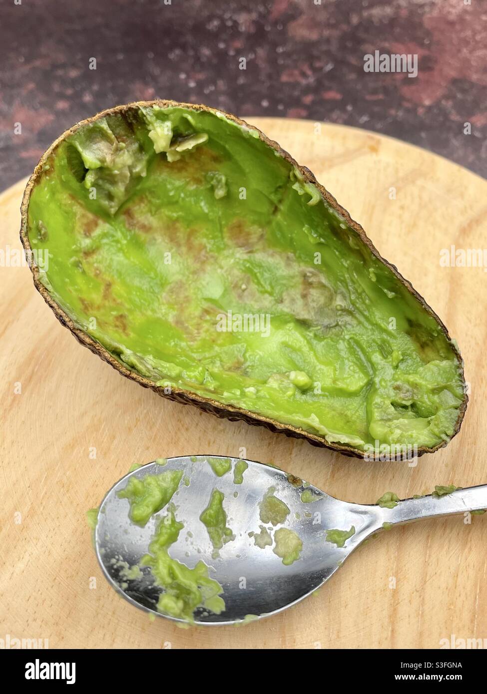 Mezzo avocado che è stato mangiato, su una tavola di legno e accanto ad un cucchiaio Foto Stock
