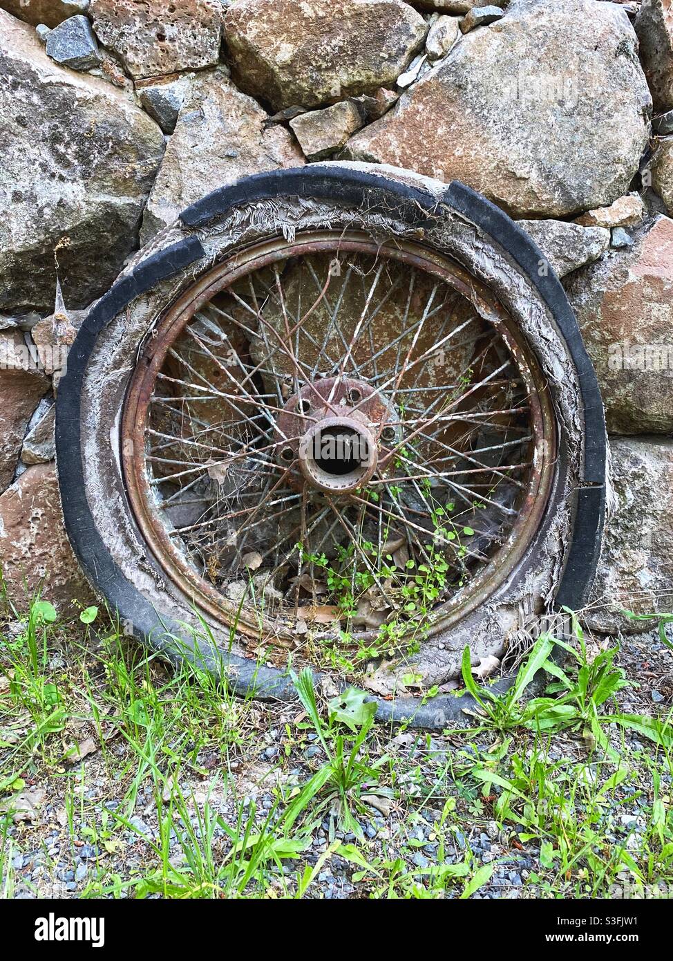 Una vecchia ruota accanto a un muro di roccia. Foto Stock