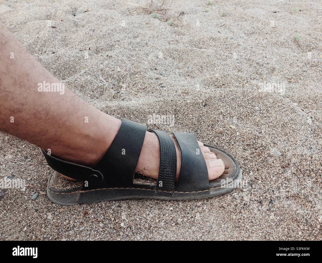 Piede di una persona sulla spiaggia sabbiosa che indossa i sandali Foto Stock