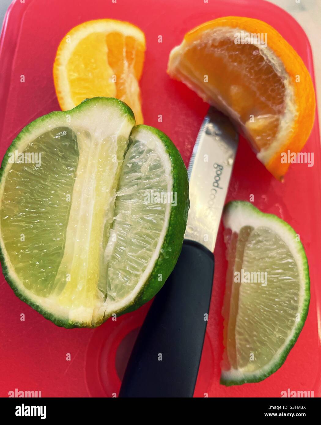 Piatto posa primo piano di un coltello di paring con limoni e lime tagliati a fette su un tagliere arancione Foto Stock