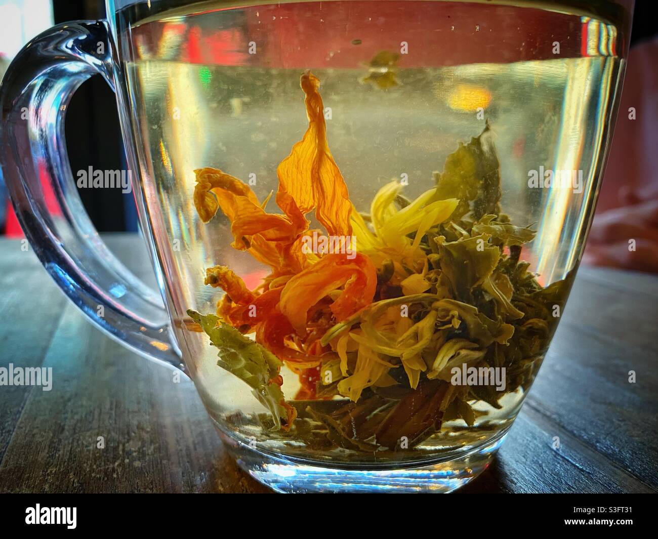 Una fotografia di tè di fiori verdi, con un fiore che si distrae delicatamente in una tazza di vetro di acqua calda. Vegan vietnamita ristorante drink - Immagine stock catturata con smartphone