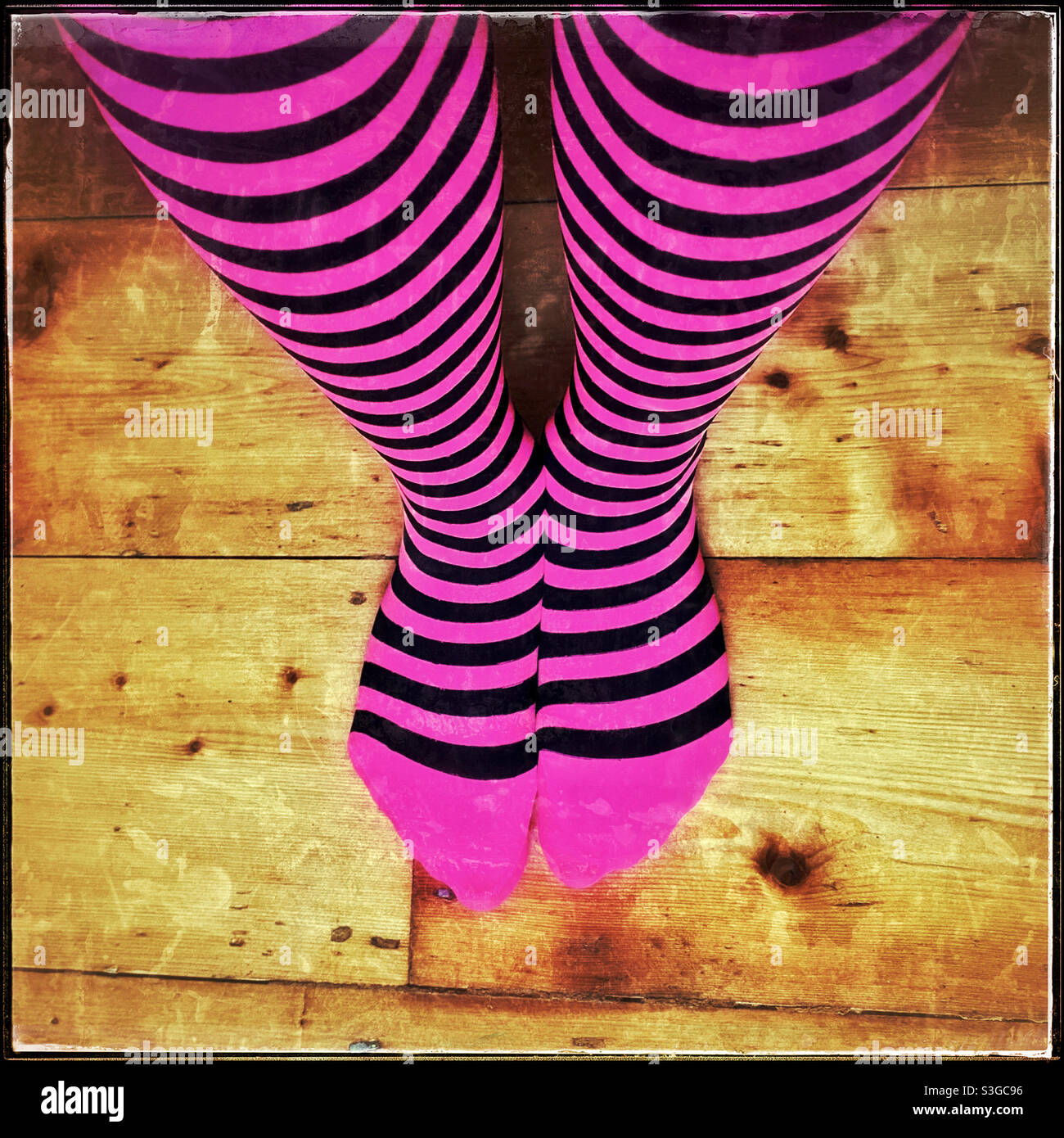 Collant a righe viola e nero che copre gambe e piedi. Guardando verso il basso i piedi che sono in piedi su pavimenti di legno. Creativo? Artistico? Colorato? Confusione? Credito fotografico - ©️ COLIN HOSKINS. - Immagine stock catturata con smartphone