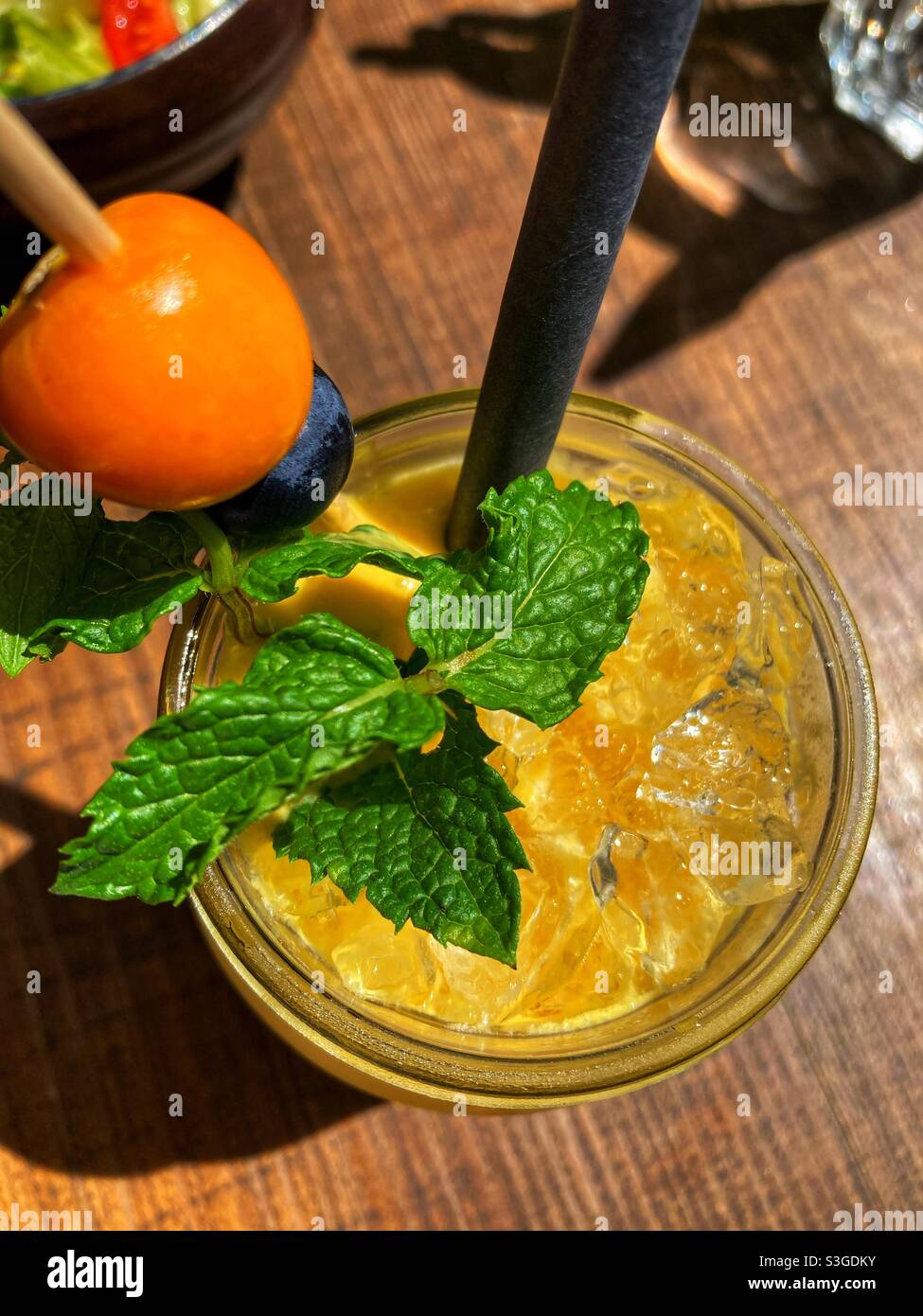 Una bevanda arancione fredda decorata con foglie di menta e una paglia di plastica Foto Stock