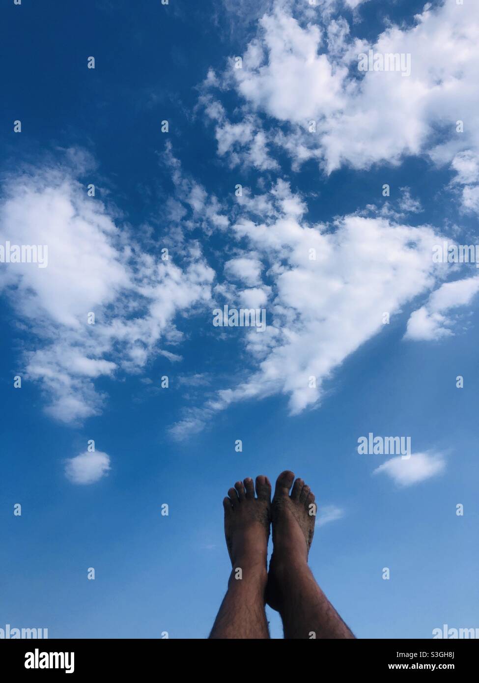 Piedi sabbiosi di una persona contro il cielo blu e le nuvole su una spiaggia Foto Stock