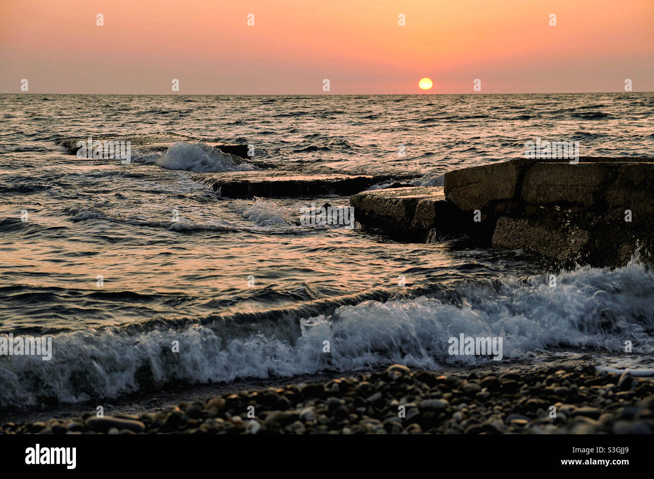 ​​wave di mare, lastre di pietra e il sole che tramonta Foto Stock