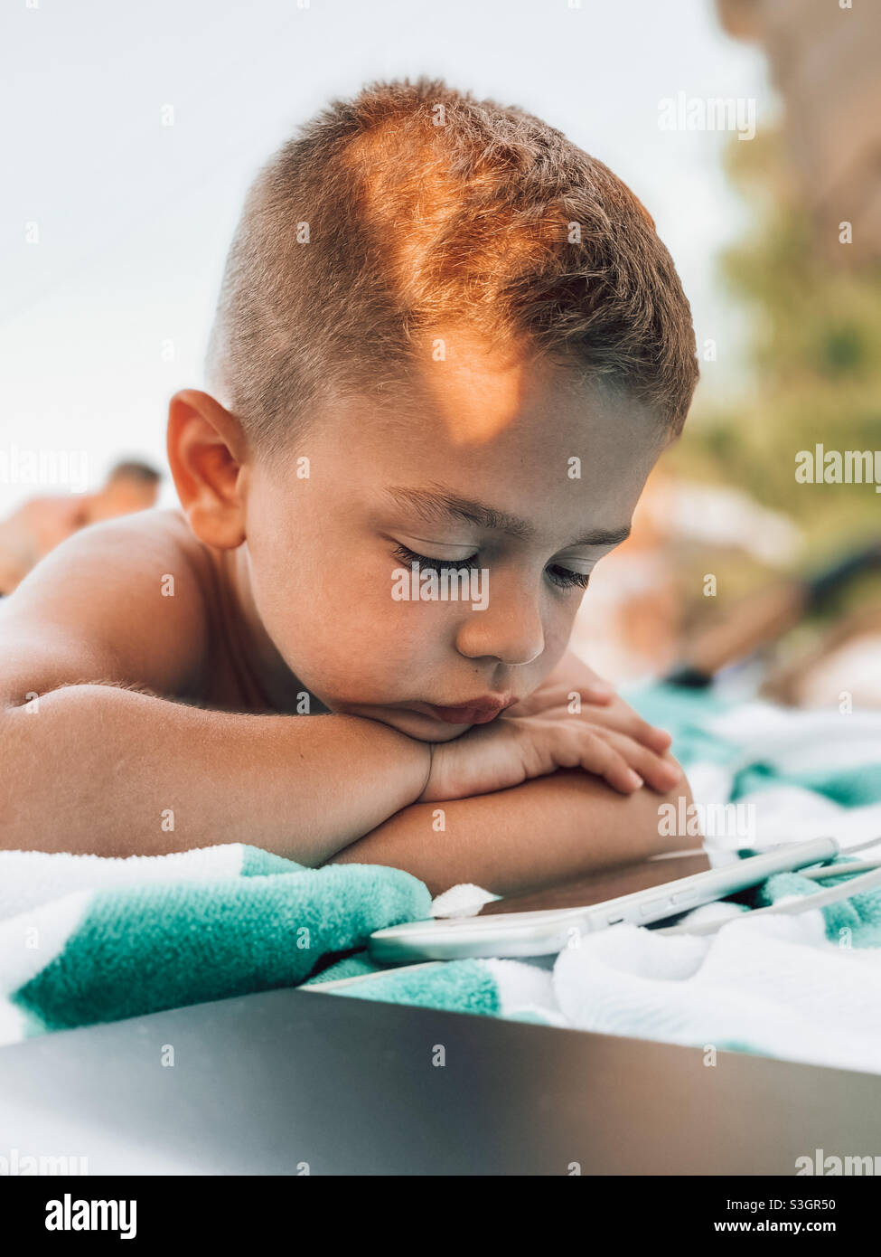 Piccolo ragazzo di cinque anni che si stesa in piscina guardando un cartone animato su un telefono Foto Stock