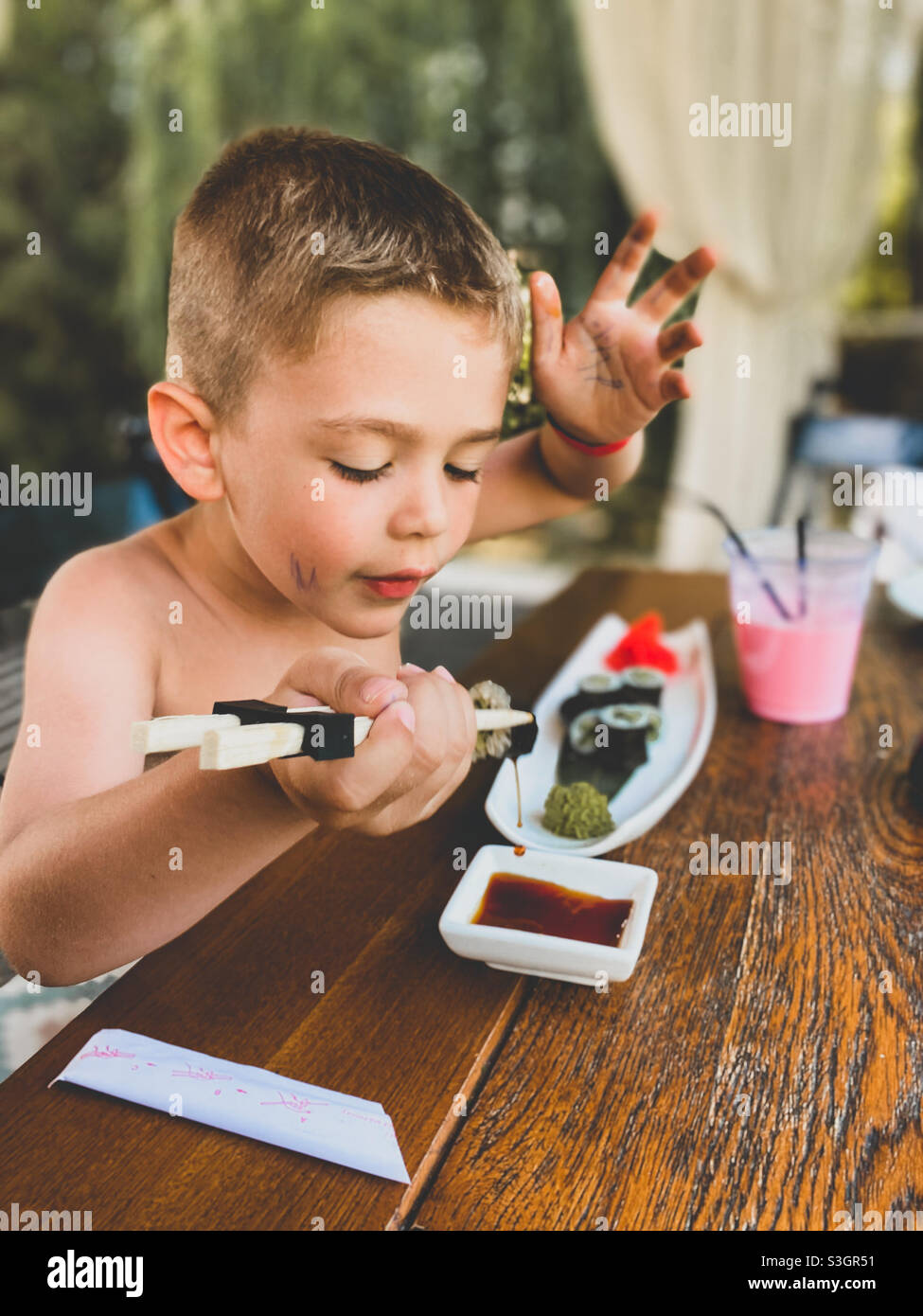 Ragazzo di cinque anni che mangia sushi e beve una frullato all'aperto Foto Stock