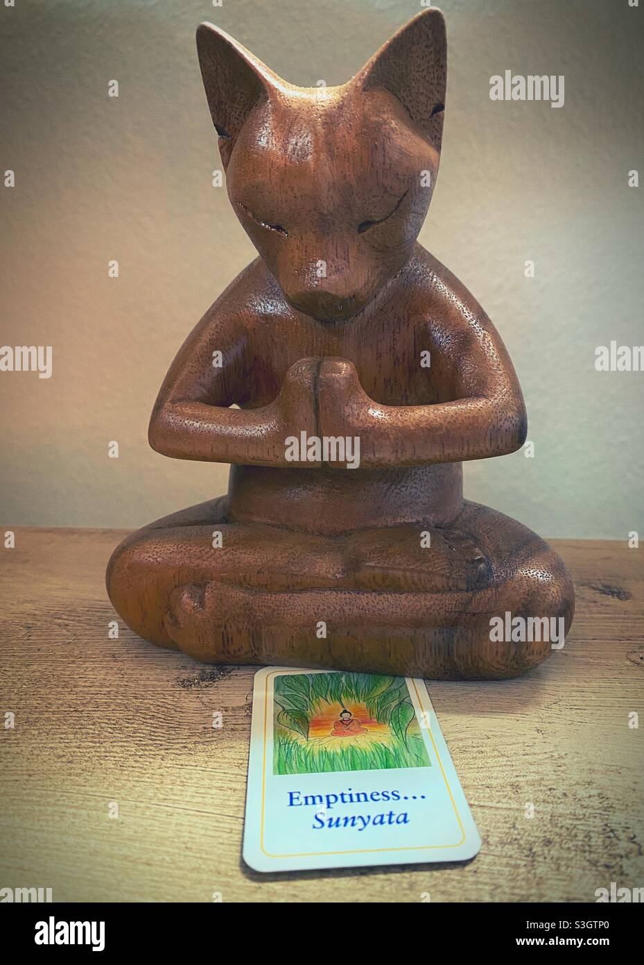 Una figurina di gatto di legno meditante e una scheda di Dharma con la parola 'vuoto'. Foto Stock