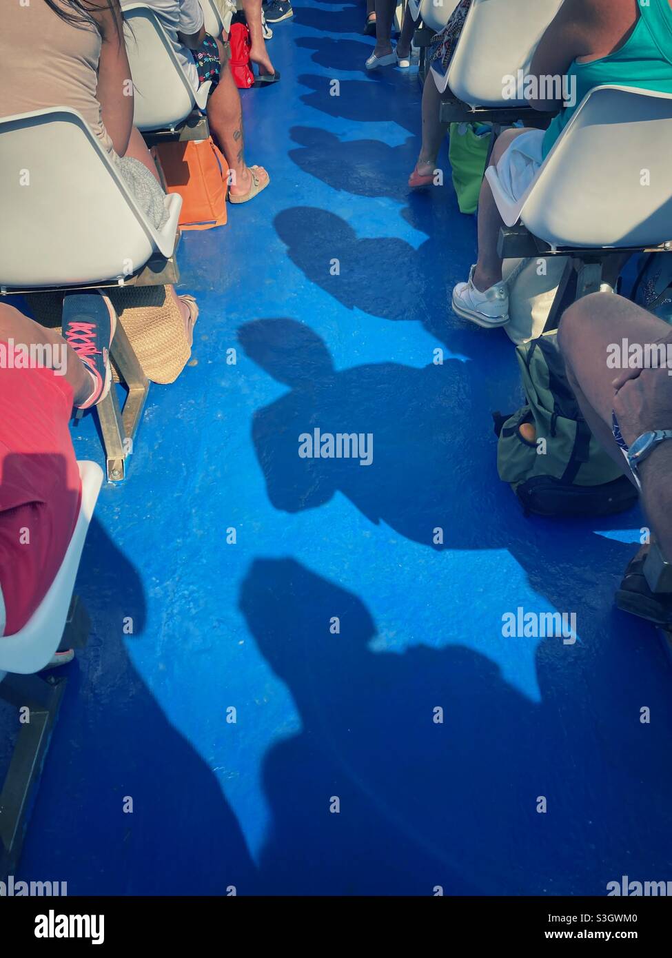 Passeggeri e le loro ombre seduti in fila su una nave passeggeri che viaggia verso le isole Tremiti sul mare Adriatico, Italia Foto Stock