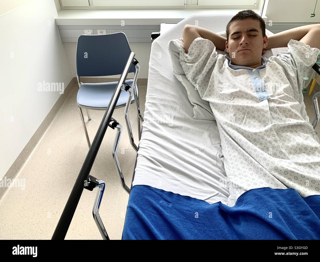 Paziente in un reparto ospedaliero coperto da una coperta. Accanto al letto c'è una sedia vuota. È in attesa di un intervento chirurgico. Foto Stock