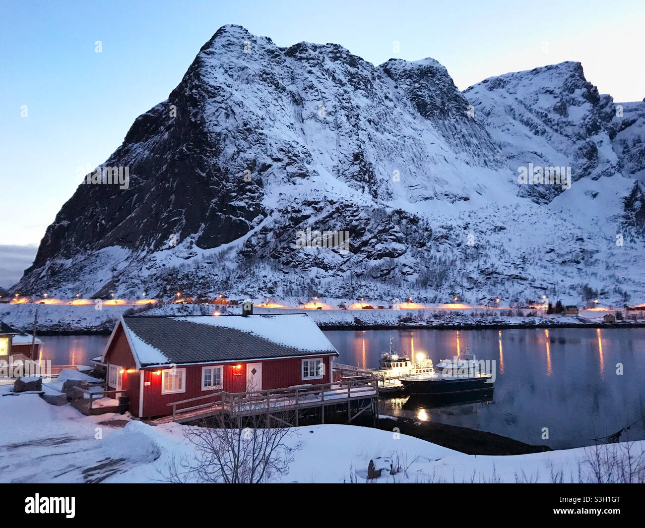 Bel villaggio di pescatori di Reine in inverno, Isole Lofoten, Norvegia. Tramonto colorato sullo splendido villaggio di pescatori di Reine, circondato da fiordo innevato. Foto Stock