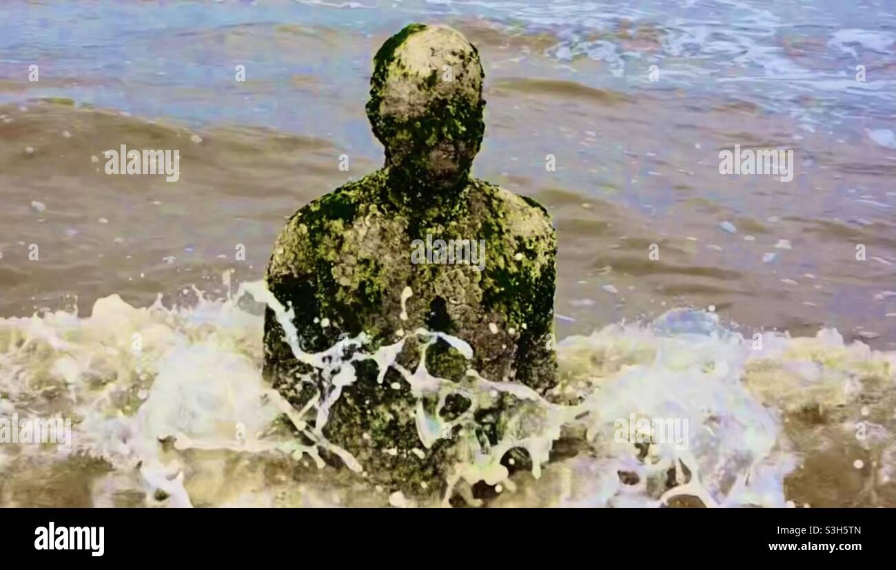 Un uomo di ferro in un altro luogo, Crosby Beach - fuori al mare che è martoriato dalle onde Foto Stock