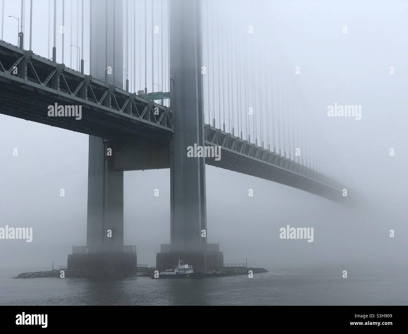 Ponte Verrazzano-Narrows in nebbia. Un battello di pattuglia NYPD sta galleggiando vicino al lato Brooklyn del ponte. Foto Stock