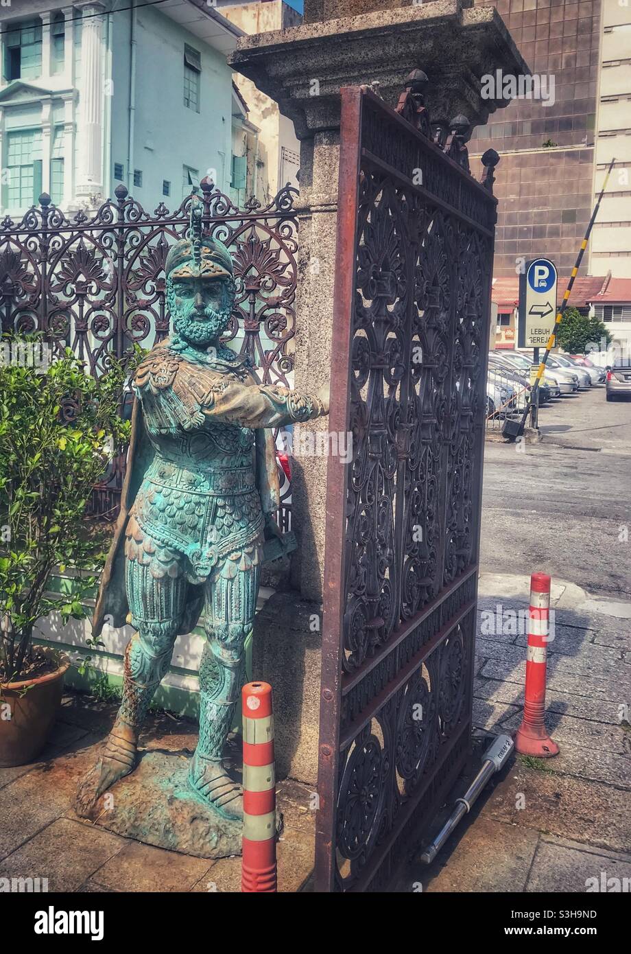 Una statua storica custodisce un cancello in ferro battuto a George Town, Penang, Malesia - Immagine stock catturata con smartphone