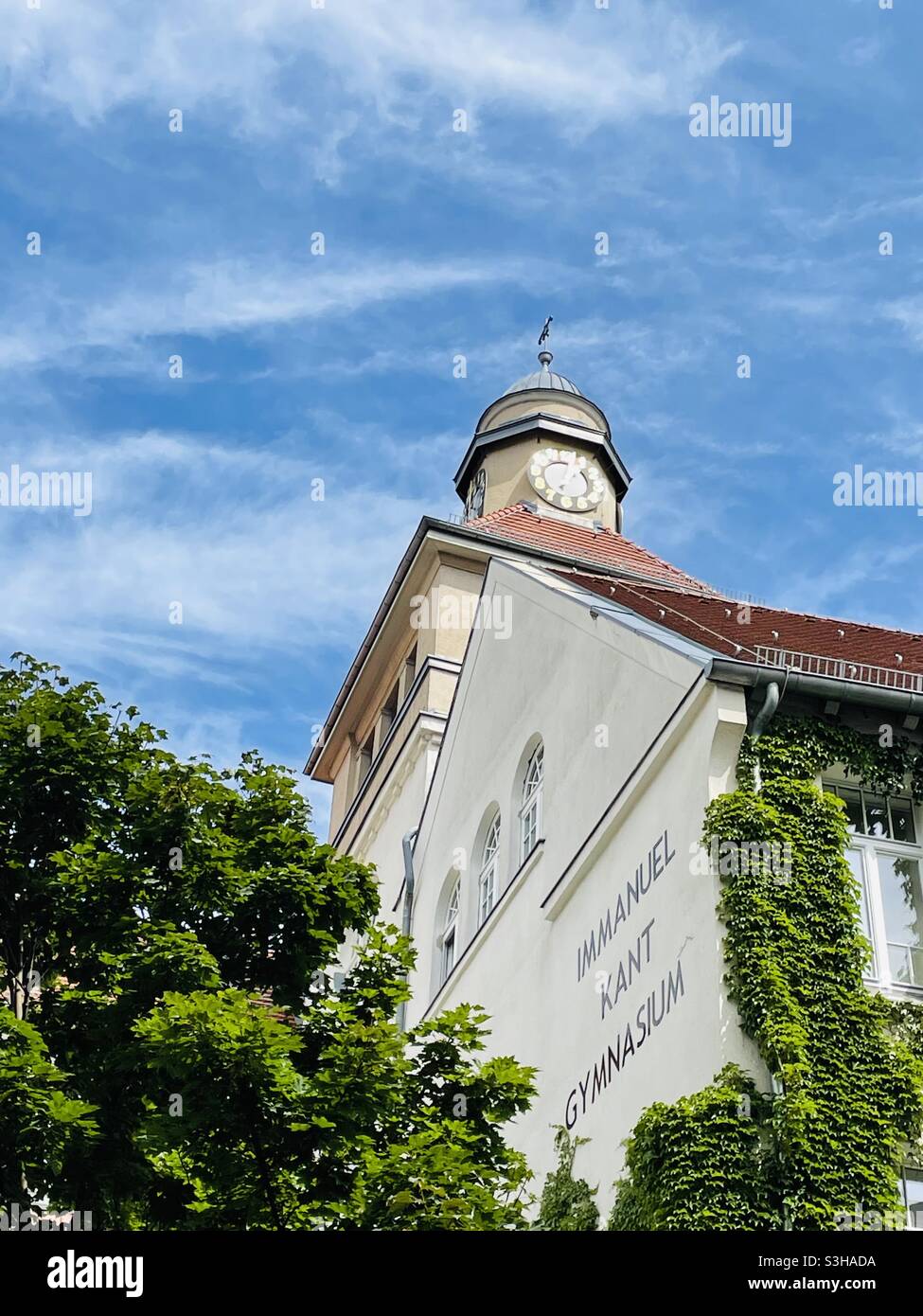 Orologio illuminato al sole sulla torre sopra la scuola superiore tedesca - Immagine stock catturata con smartphone
