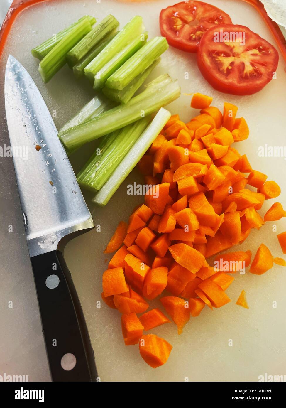 Primo piano di verdure tagliate a dadini e un grande coltello su un piano di taglio residenziale da cucina, USA - Immagine stock catturata con smartphone