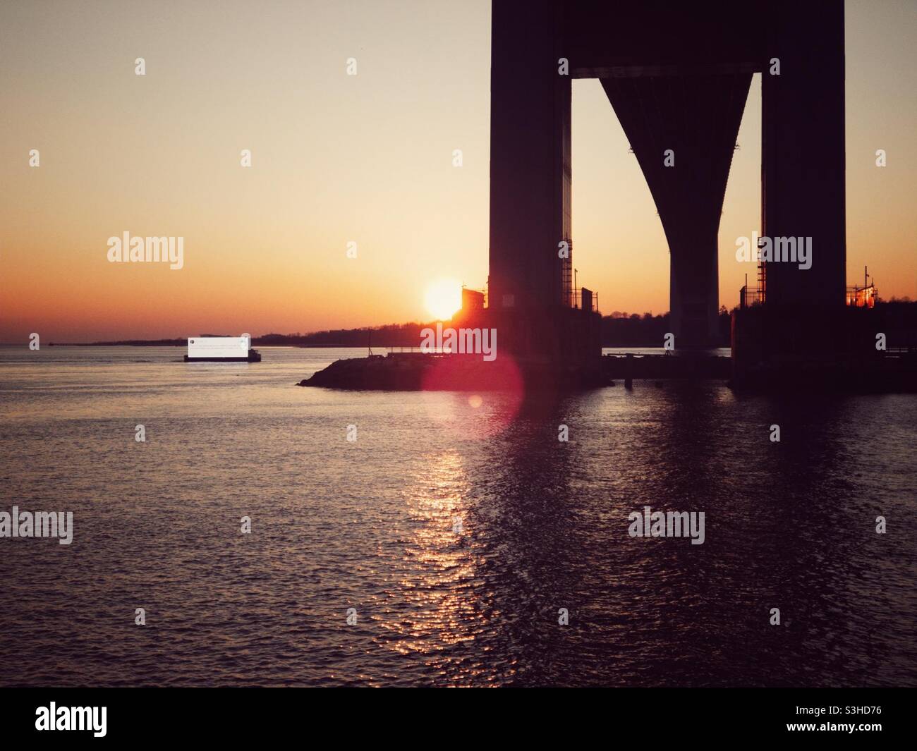 Cartellone digitale galleggiante sotto il ponte Verrazzano-Narrows a Brooklyn, New York al tramonto. Foto Stock