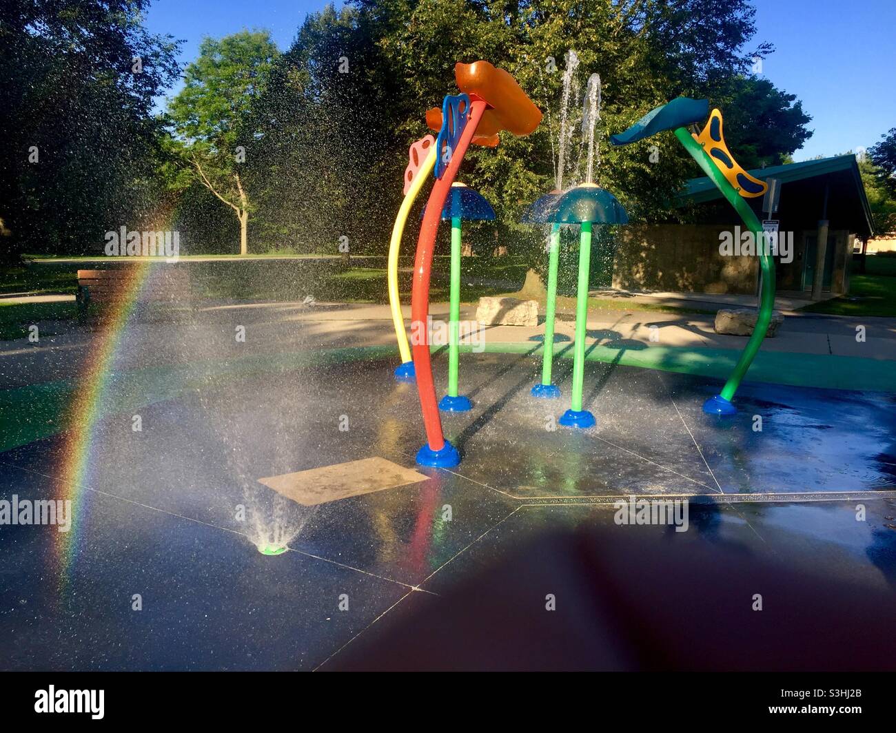Arcobaleno, spruzzi d'acqua e cascata. Splash pad con colorate fontane d'acqua, una moderna fairyland in un grazioso parco, Ontario, Canada. Luogo popolare per rinfrescarsi e divertirsi in primavera, estate e autunno. Foto Stock