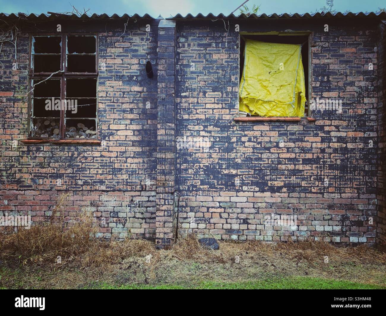 Una fotografia del lato di un edificio abbandonato con grotty muratura antica e telone giallo nella finestra - Immagine stock catturata con smartphone