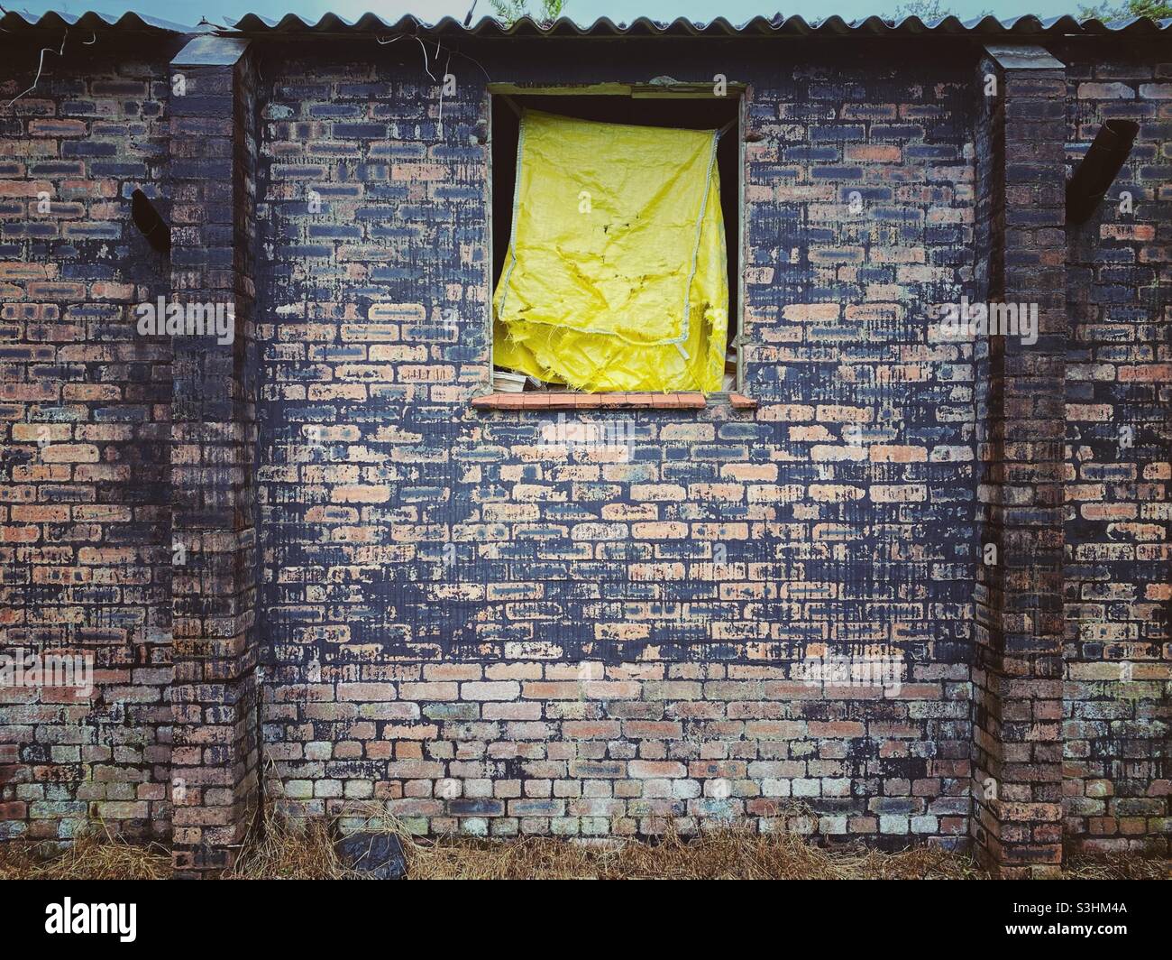 Una fotografia del lato di un edificio abbandonato con grotty muratura antica e telone giallo nella finestra Foto Stock