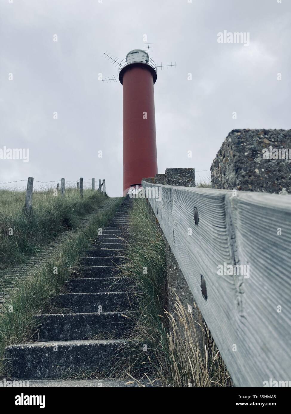 Una scala con corrimano in legno conduce ad un faro rosso su una collina erbosa a Julianadorp, Olanda - Immagine stock catturata con smartphone