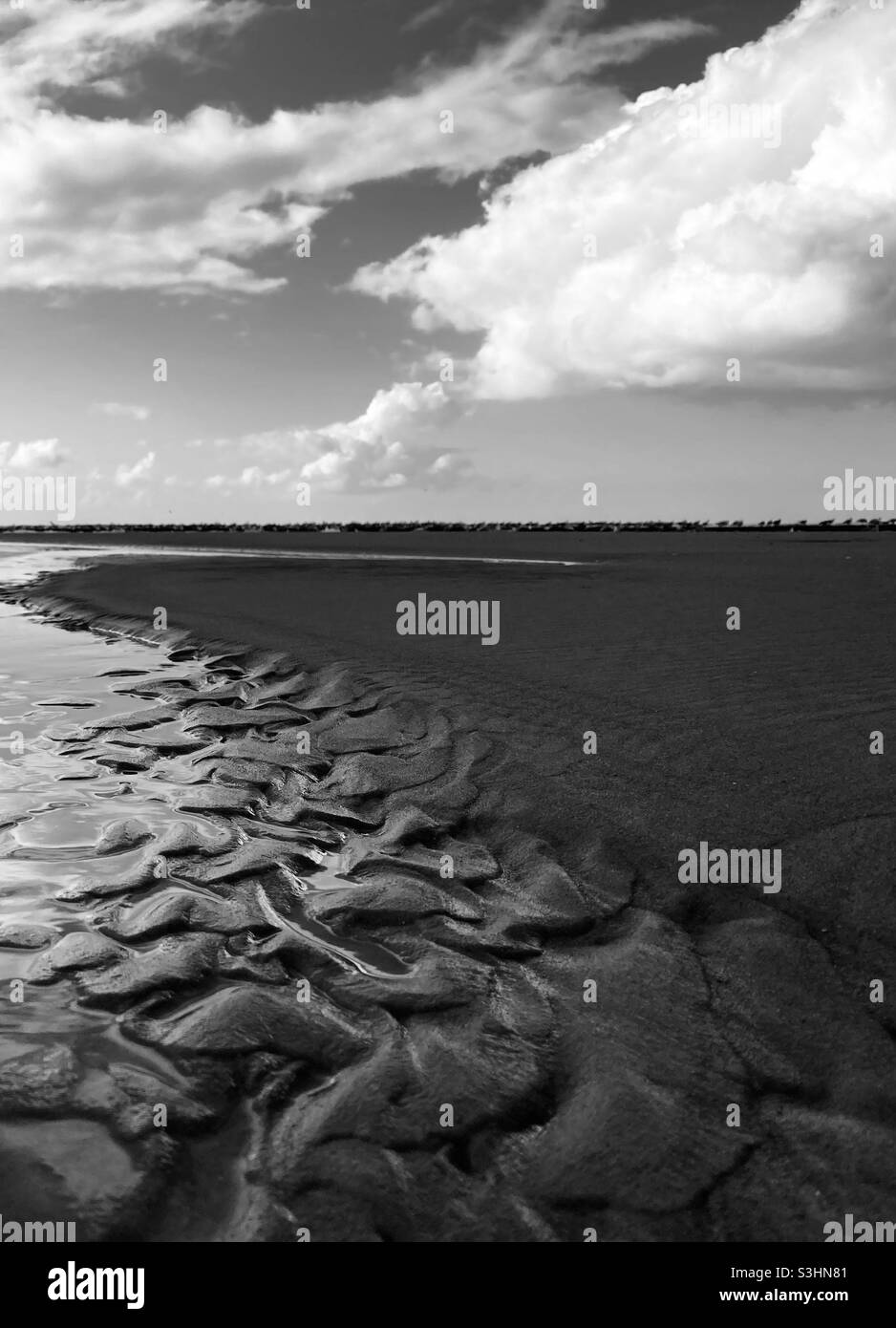 Motivi creati dal vento e dalle onde nella sabbia sulla spiaggia con le nuvole nel cielo Foto Stock