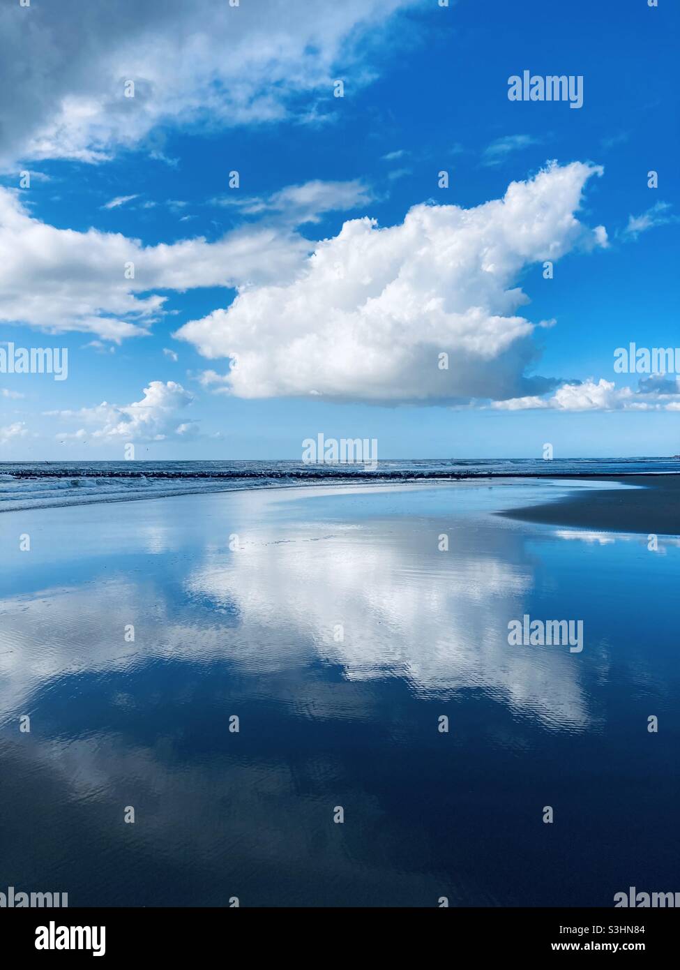 una nuvola bianca brillante nel cielo blu si riflette sulla superficie liscia dell'acqua vicino al mare Foto Stock