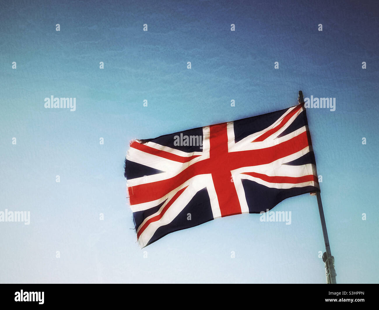 La bandiera del Regno Unito soffia orgogliosamente in un cielo blu con una grande retroilluminazione. Foto ©️ COLIN HOSKINS. Foto Stock