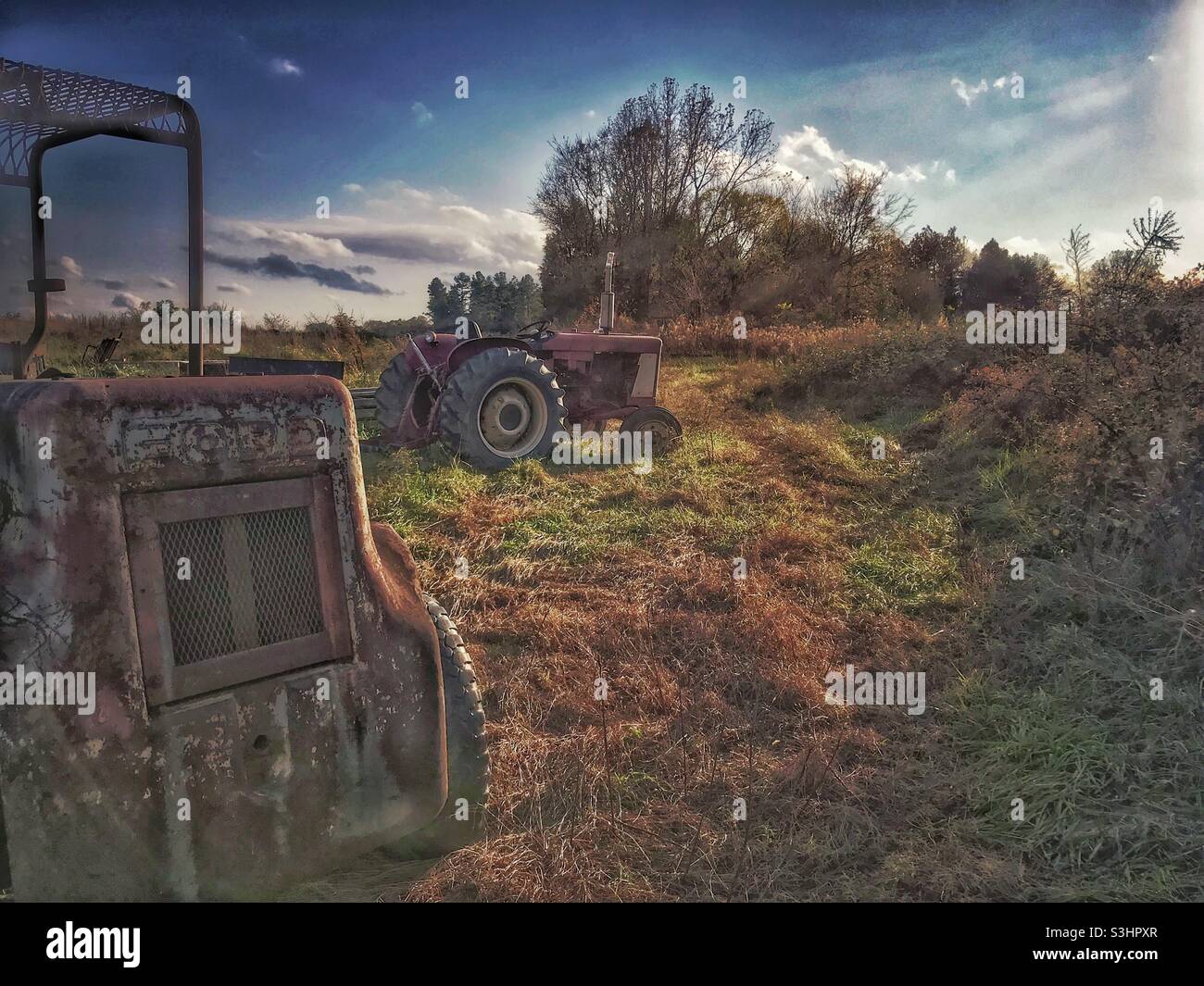 Vecchio carrello elevatore e trattore alla luce del sole di sera sulla fattoria Foto Stock